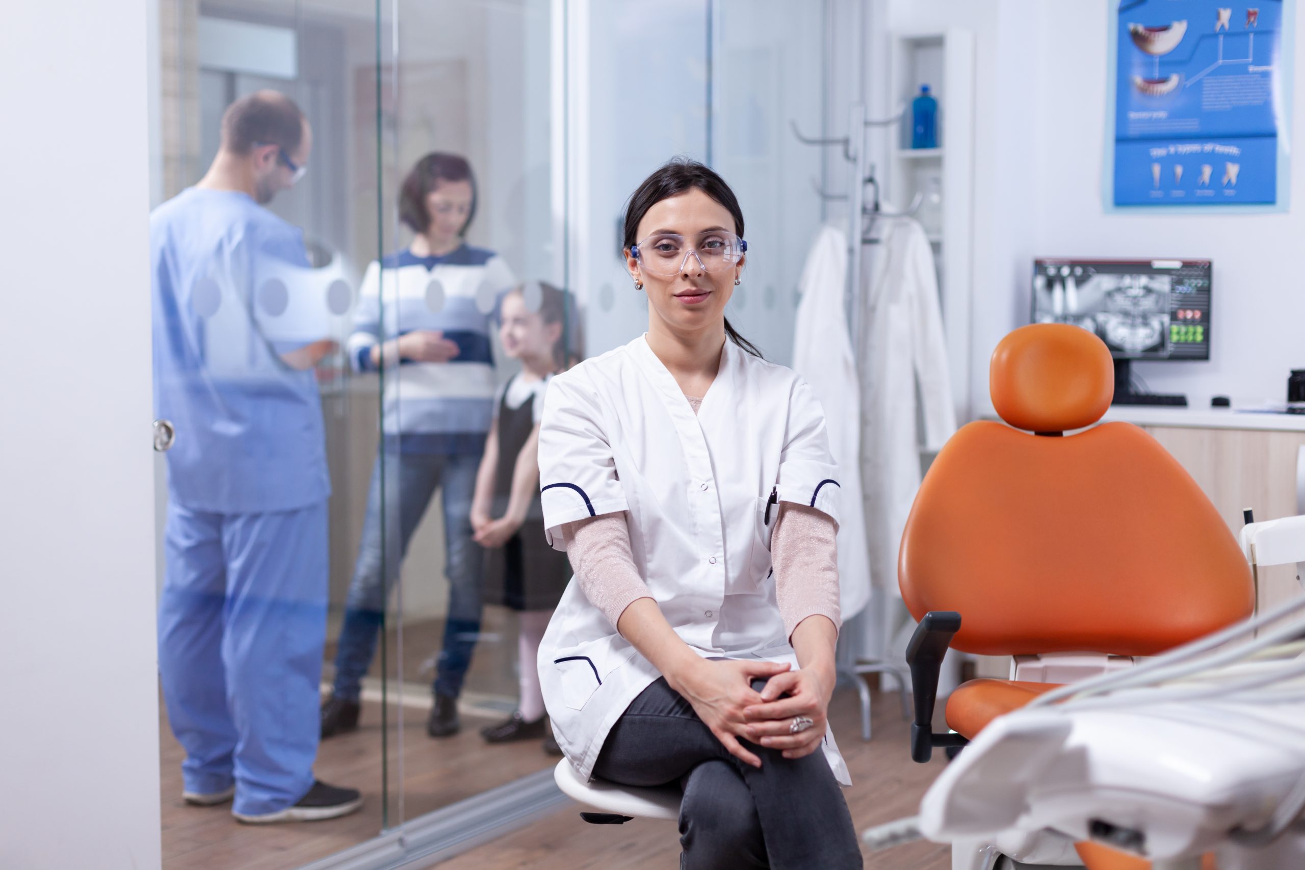 Portrait d'une dentiste tenant un modèle de crâne et expliquant les règles d'hygiène des dents au patient assis dans un fauteuil dentaire